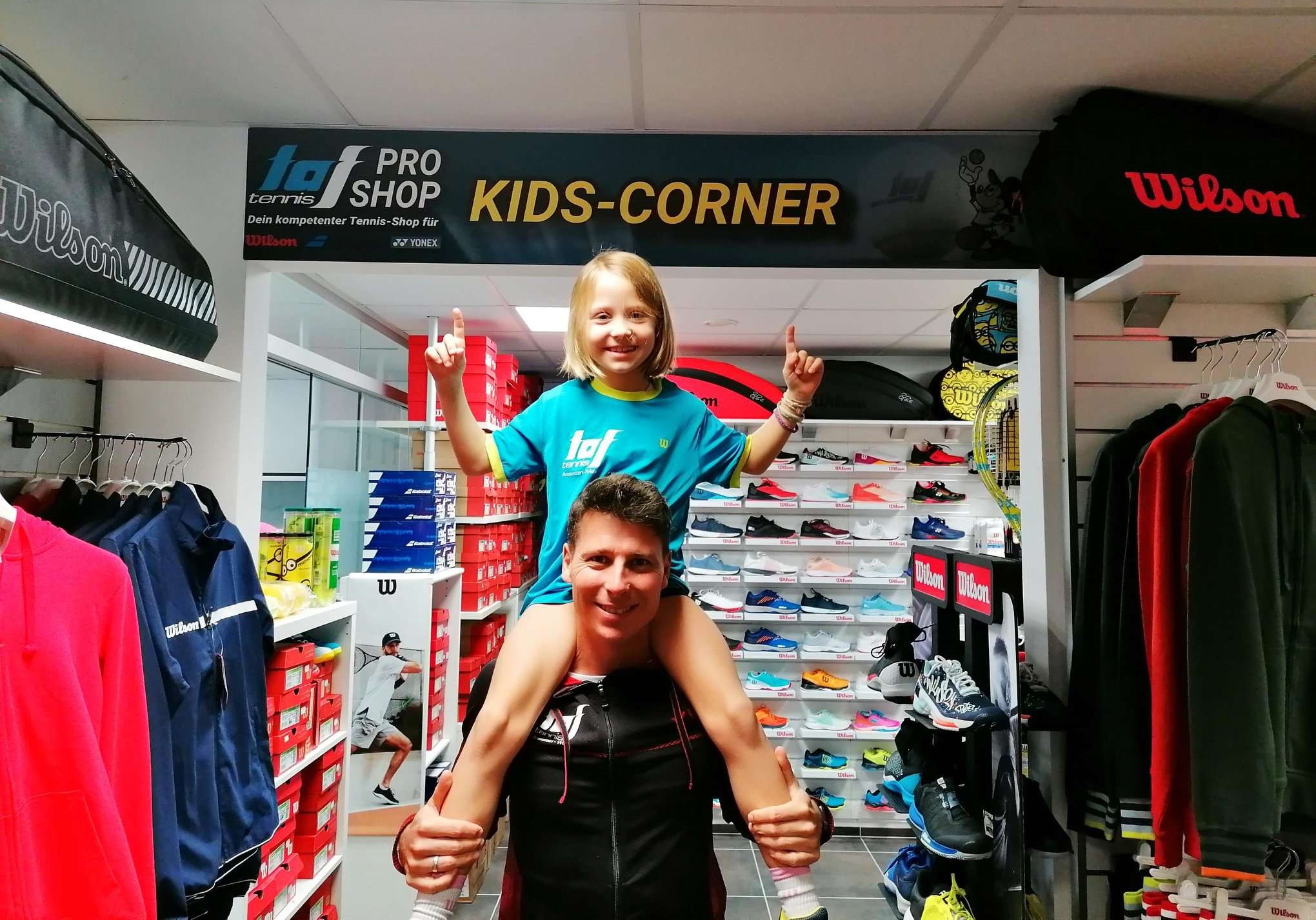 Tenniskind auf den Schultern vom Papa zeigt auf den neuen Kids-Corner im taf-tennis Pro Shop